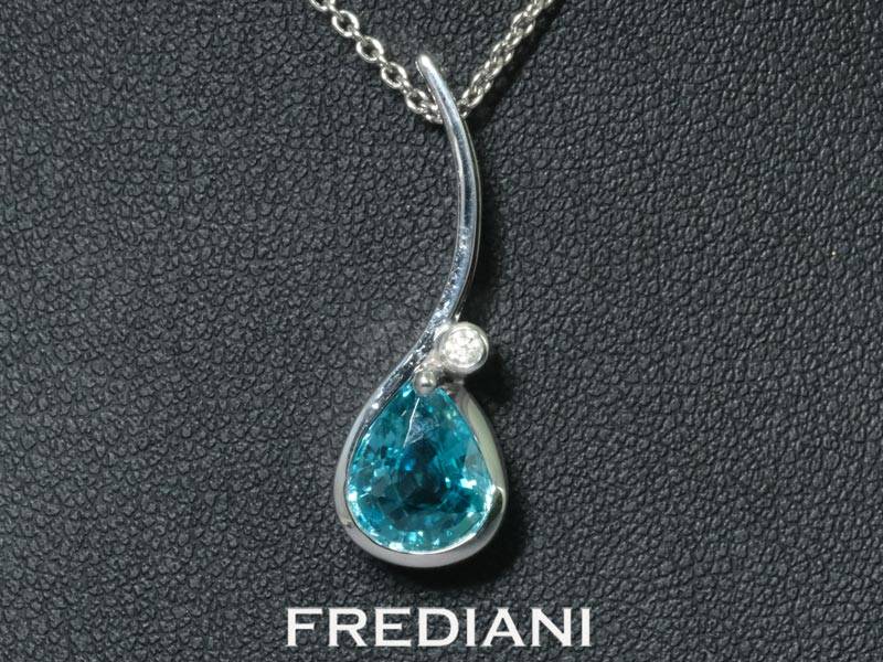 Pendentif en or blanc 750/000 serti d'un zircon bleu en forme de poire accompagné d'un diamant rond naturel.