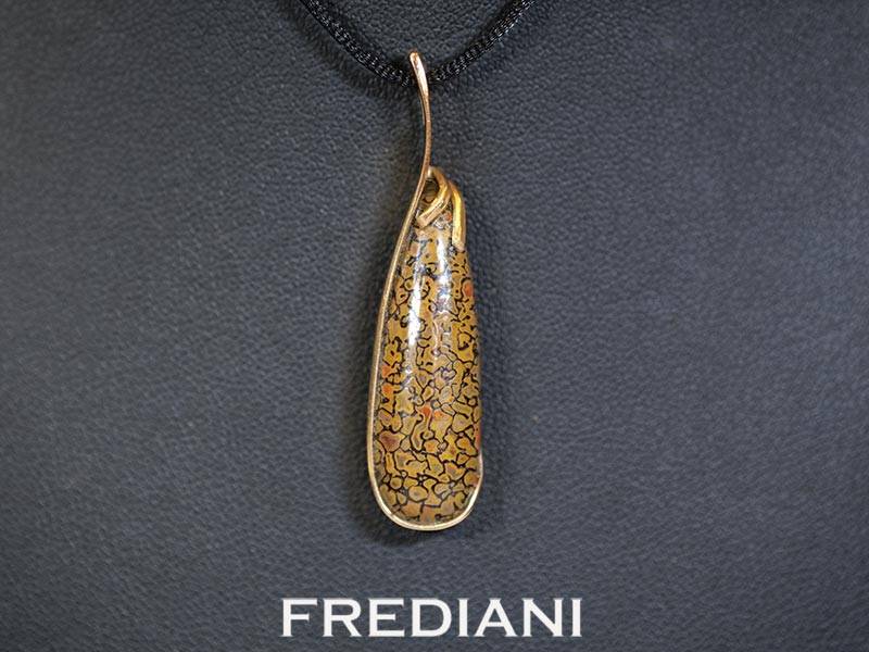 Pendentif en or jaune 750/000 serti d'un cabochon en os de dinosaure pétrifié.