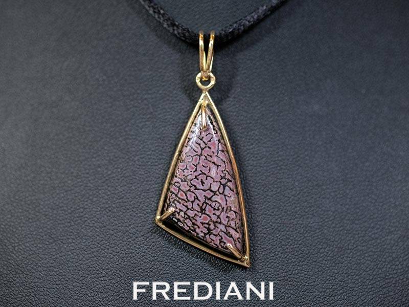 Pendentif en or jaune 750/000 serti d'un cabochon en os de dinosaure pétrifié.