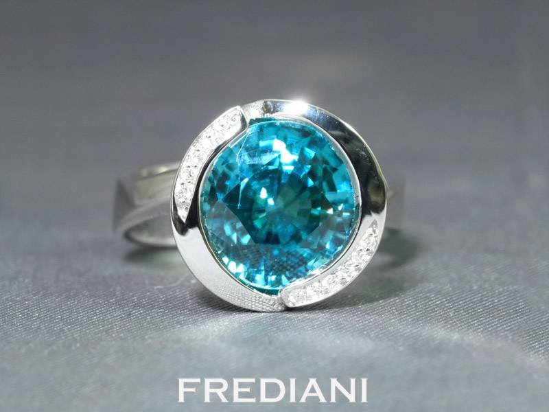 Bague en or blanc 750/000 sertie d'un magnifique zircon bleu rond et accomopagné de 12 diamants naturels.