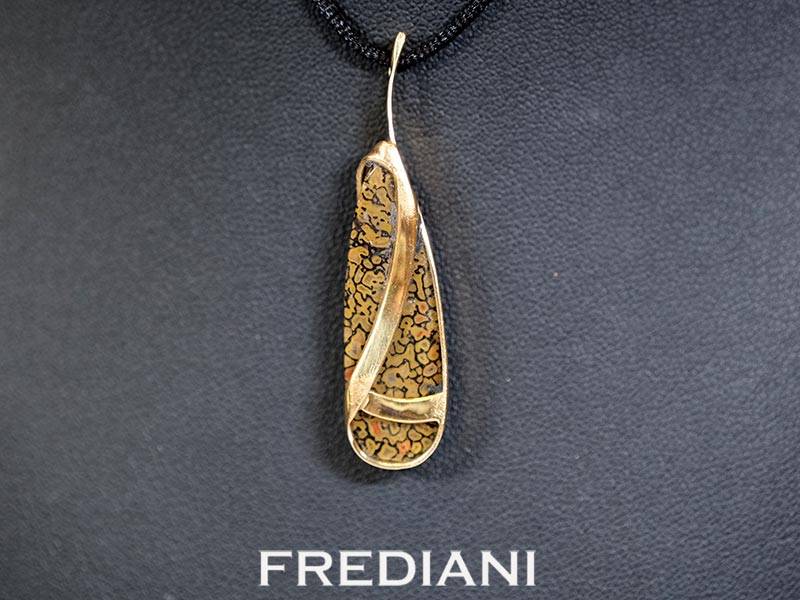 Pendentif en or jaune 750/000 serti d'un cabochon en os de dinosaure pétrifié.