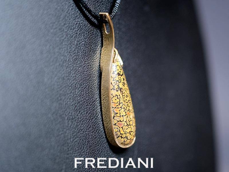Pendentif en or jaune 750/000 serti d'un cabochon en os de dinosaure pétrifié.