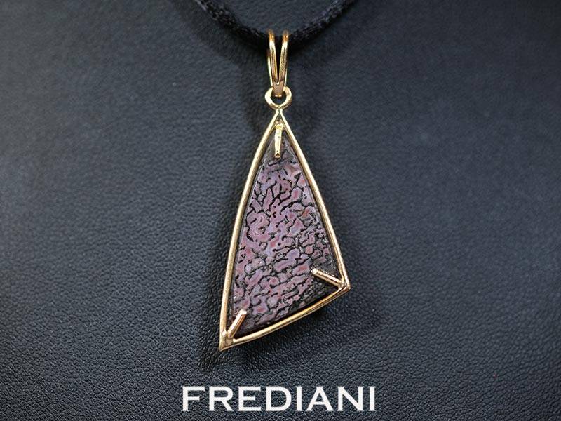 Pendentif en or jaune 750/000 serti d'un cabochon en os de dinosaure pétrifié.